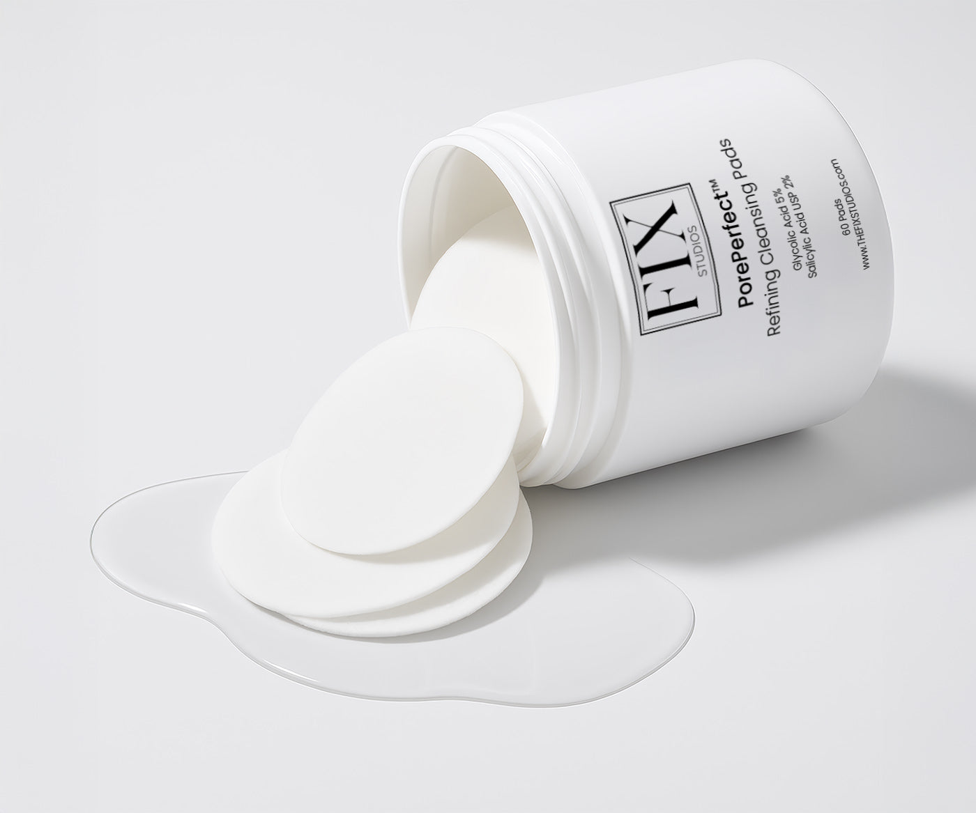 A jar of Fix Studios PorePerfect™ Refining Cleansing Pads Medical-Grade Acne Product lays on its side with pads and liquid spilling out onto the surface