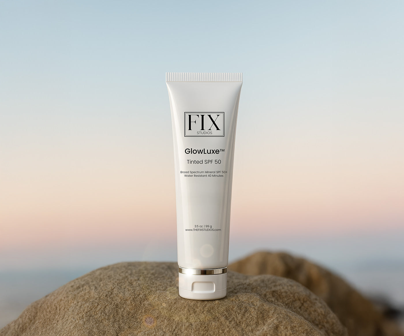 A bottle of Fix Studios medical-grade GlowLuxe™ Tinted SPF 50 sunscreen rests on the beach