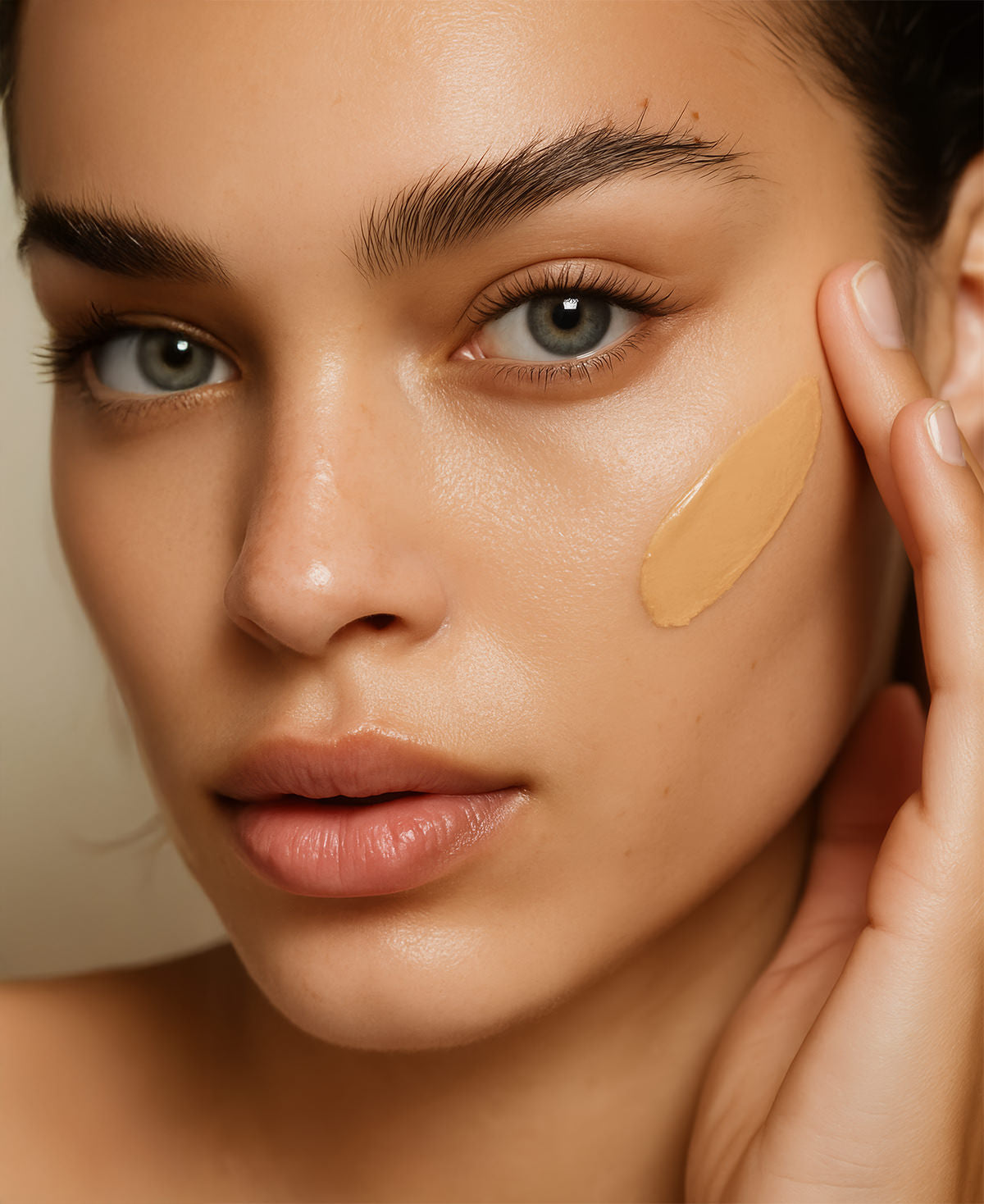 Close of up a beautiful woman applying Fix Studios medical-grade GlowLuxe™ Tinted SPF 50 sunscreen to her cheek.