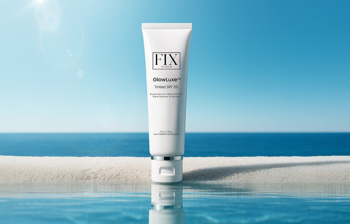 A bottle of Fix Studios medical-grade GlowLuxe™ Tinted SPF 50 sunscreen rests on the beach