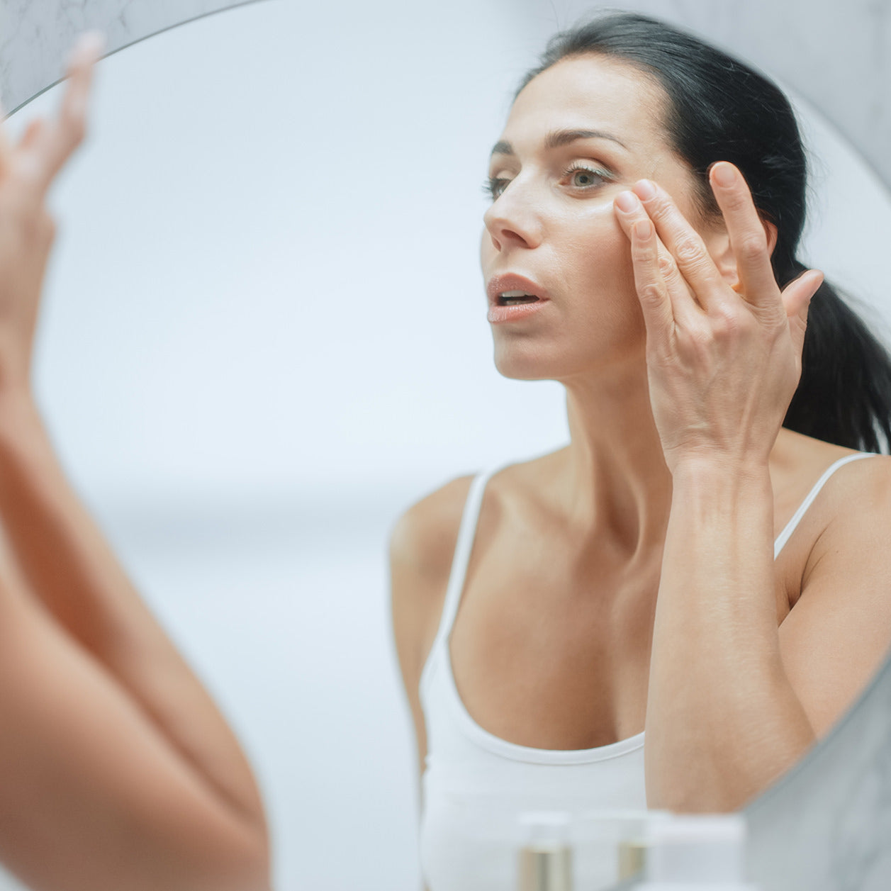 A woman who participates in Fix Studios medspa Cincinnati Mason OH progressive beauty evolution program applies skincare product to her cheekbone while looking in the mirror